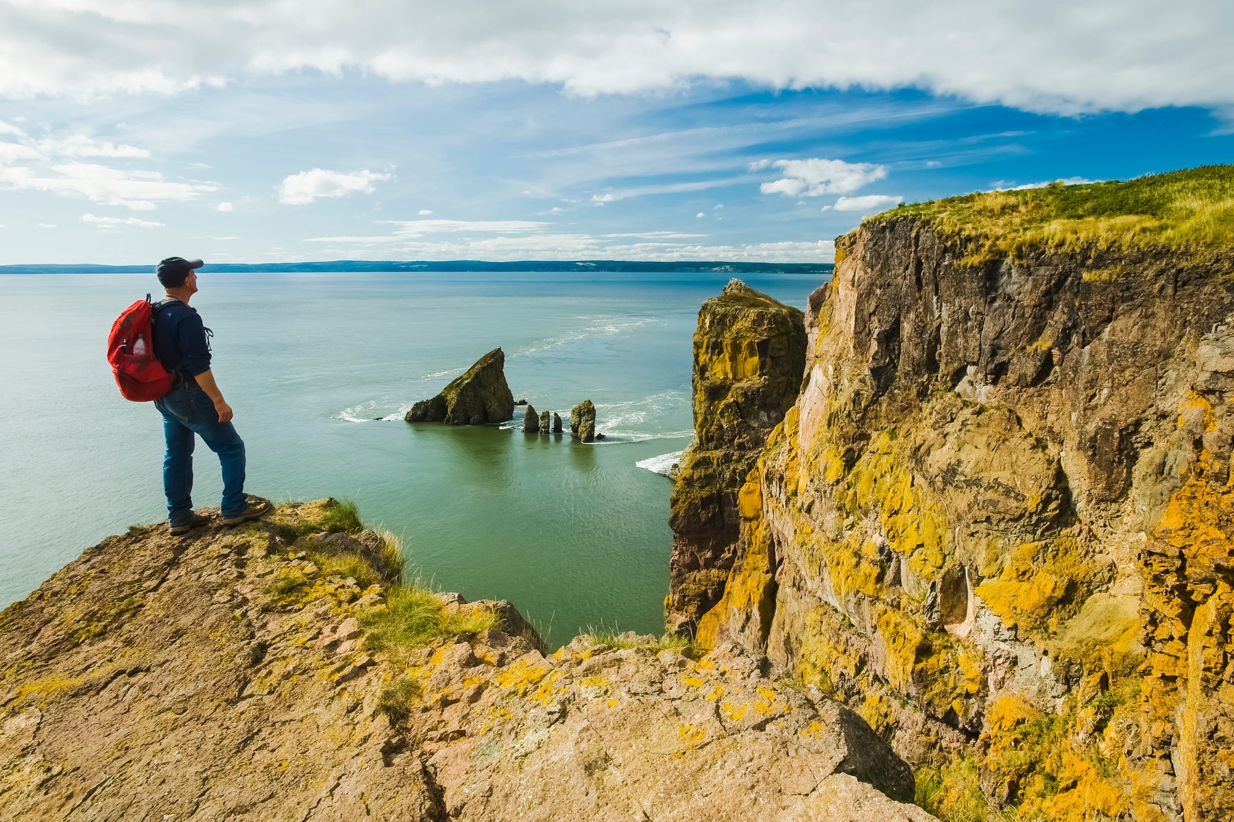 A hiker stands on a cliff edge looking over the Bay of Fundy in Nova Scotia