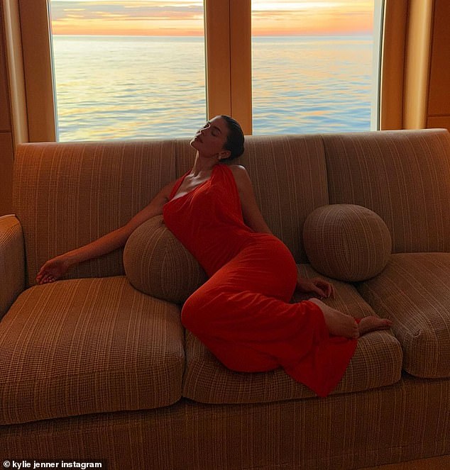 She also donned a fitted, reddish-orange maxi dress as she quickly paused for a photo while lounging on a comfy couch inside what appeared to be the cabin of a boat